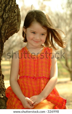 Little girl sitting in a tree for a portrait with her hair blowing.