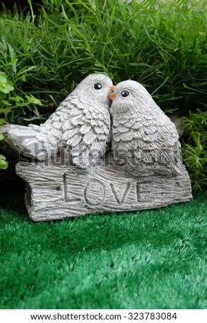Kissing birds stone statue and Love word with green tree background.