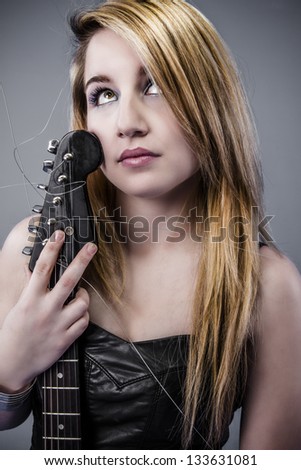 Sexy young blonde dressed in black leather holding black electric guitar with thoughtful look