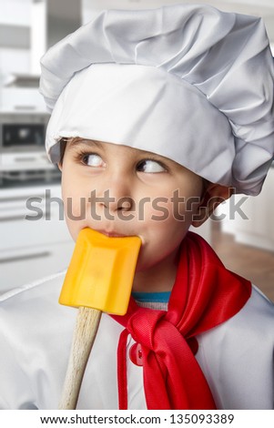 Funny boy dressed in chef with orange spoon in mouth