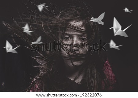 Teenage girl with hair in the wind and birds head paper, origami