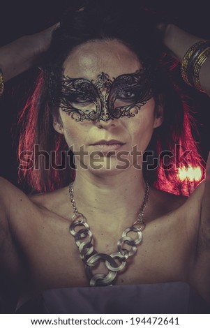 Mask brunette woman with golden jewelry and red light on hair