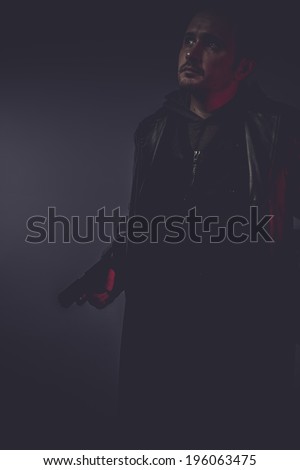 portrait of stylish man with long leather jacket, gun armed