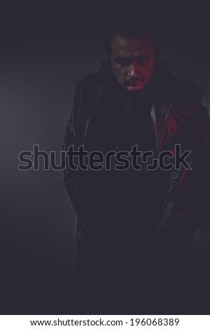 shadow portrait of stylish man with long leather jacket, gun armed