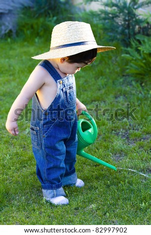 little baby gardener lost in his task at hand with his hat on and watering the plants like a professional