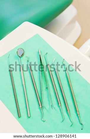 stainless steel dental surgery instruments for teeth care lying on a green bib (dental chair arm)