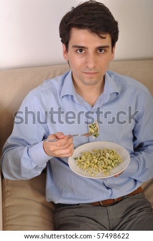 attractive young man sitting on the couch eating lunch (pasta with chicken)