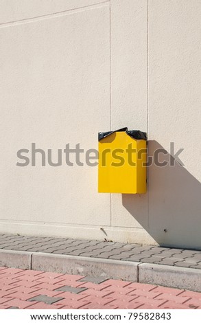 yellow garbage can hanging on wall at a urban sidewalk