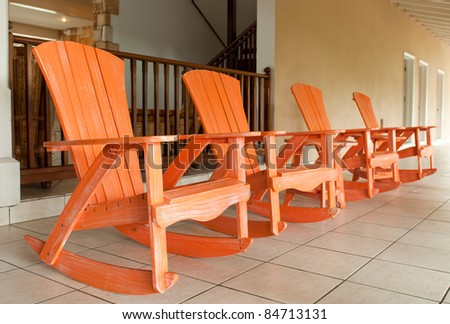 row of orange wooden rocking chairs on a porch