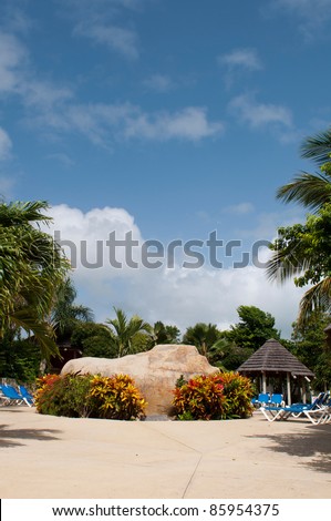 gorgeous swimming pool area with big artificial stone, chairs and bungalow on a tropical resort (surrounded by palm trees)