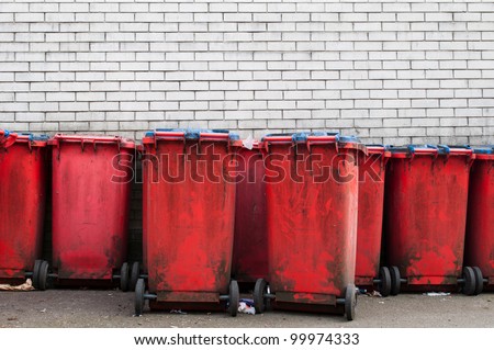 many red dirty garbage bins against a grey brick wall (copy-space available)