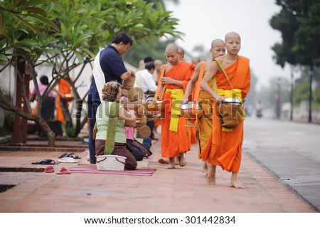 LUANG PRABANG, LAOS- JULY 7, 2011 : Monks gathering morning alms in Luang Prabang.The tradition of giving alms to monks in Luang Prabang has been extended to tourists.