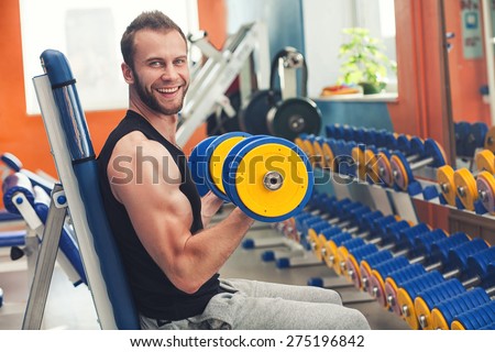 Young smiling athlete lifting weights in the gym