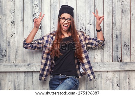 Hipster girl in glasses and black beanie show victory sign on the wooden background
