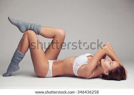 beautiful young girl in white lingerie and long grey socks lying on a light background