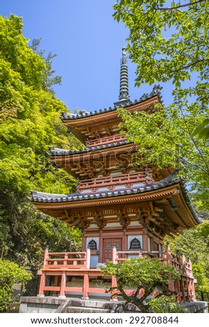 Three storey Japanese style temple pagoda with green maple tree and blue sky at summer.