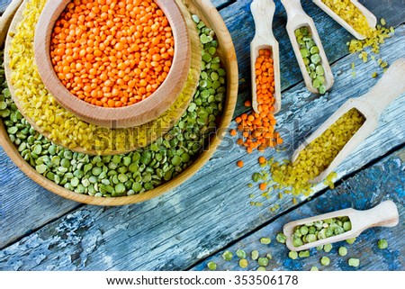 Colorful variety of cereals in a bowls and scoops on wooden background. Red lentils, yellow bulgur and green dried peas