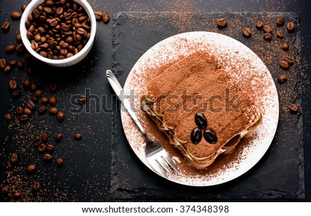 Delicious Italian dessert tiramisu with chocolate, cocoa and coffee beans on a black background. Top view with copy space