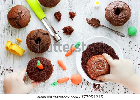 Easter carrot cakes cooking Kid hands decorated cupcakes chocolate sprinkles on a white table. Creative Easter baking, cooking process with a child in the kitchen