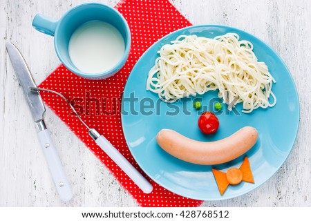 Dinner or breakfast for kids - spaghetti with sausage and vegetables in the shape of clown face. Creative food art idea for children meal top view