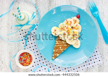 Dessert or breakfast for kids - pancake with banana and colorful sugar sprinkling in the shape of ice cream cone. Creative food art idea for children meal top view