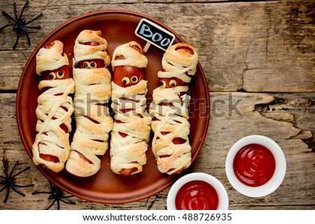 Sausage mummies in dough scary halloween food celebration party with funny eyes on vintage wooden background
