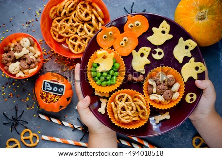 Child hands puts on the table plate with variety of treats at Halloween theme party top view