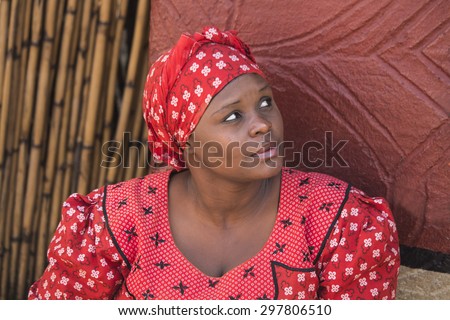 South Africa, Gauteng, Lesedi Cultural Village (unique center of African culture) - 04 July, 2015 . Close-up portrait of Zulu woman Bantu in handmade red dress and african hat next to her house.