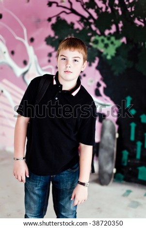 Young boy with shoulder bag and skateboard and graffiti wall in background