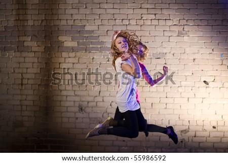 Teenage girl jump in the air against brick wall urban style lit with flash