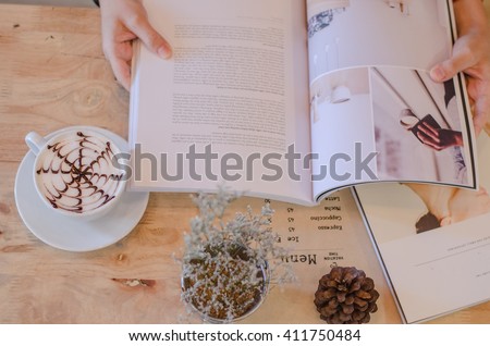 Female reading magazine and drink coffee on wooden table from above