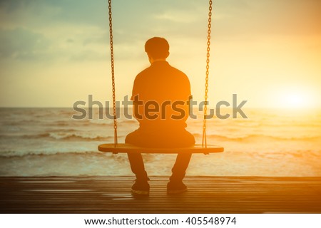 Single man alone while swinging on the beach at sunset