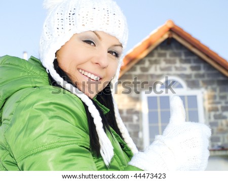 woman in winter clothes showing ok sign in front of house