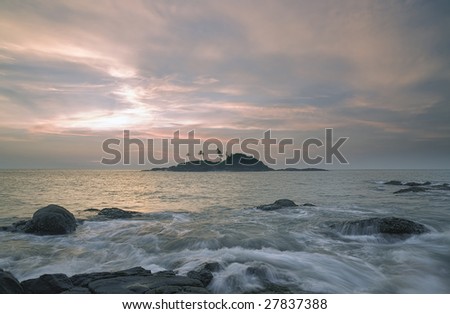 Tropical island with palm trees at sunset in the ocean with the waves and the rocks on perdnem plan