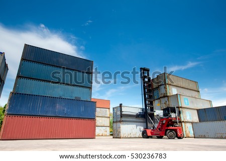 Forklift truck lifting cargo container in shipping yard or dock yard against blue sky with cargo container stack in background for transportation import,export and logistic industrial concept