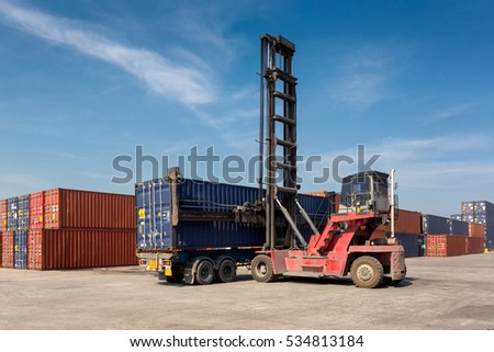 Forklift truck lifting cargo container in shipping yard or dock yard against blue sky with cargo container stack in background for transportation import,export and logistic industrial concept