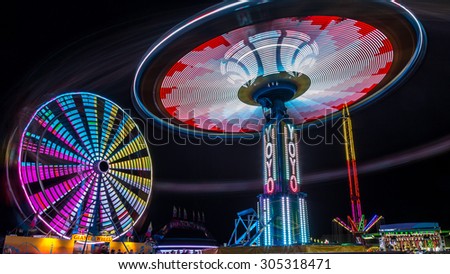 Giant Ferris Wheel and Yo-Yo amusement ride side by side in night time shot with long exposure.