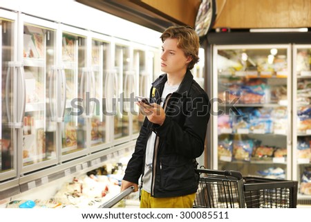 Young man choosing frozen food from a supermarket freezer. Checking list.