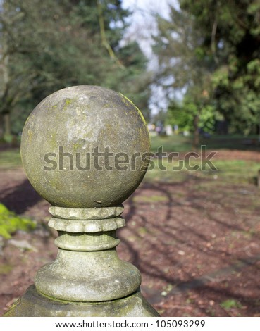 Old weathered moss covered stone ball sculpture with a background of a lawn and trees