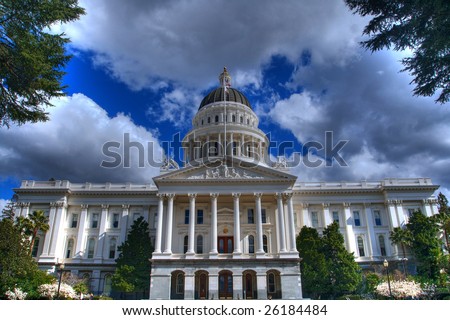 an high dynamic range image of the California State Capital Building from a distance bordered by trees and a blue sky with grey and white clouds