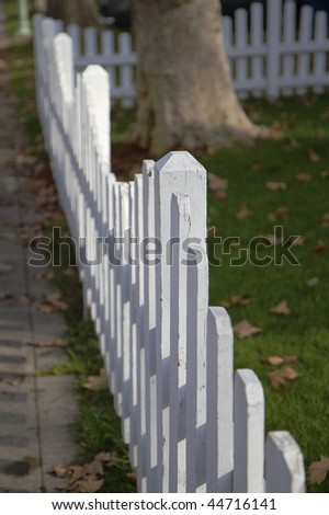 White picket fence in perspective bordered by sidwalk and yard