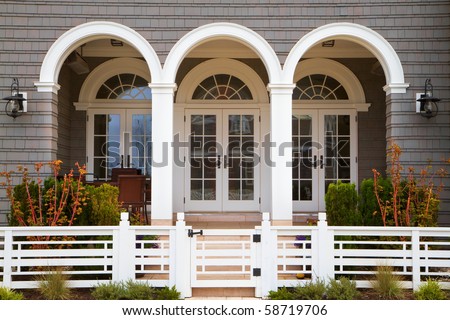 Three french door entrance to grey house with white trim and deco style fence