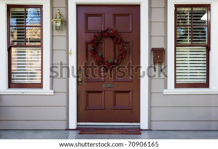 Home burgundy door with wreath with two white trimmed blinded windows
