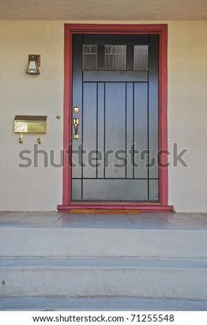 Black door with brass fitting with burgundy trim on a beige stucco house