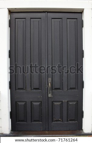 Pair of old wood black doors on the white wall of a church