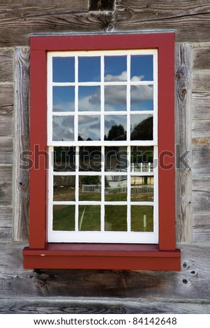 Red framed white window on an old wood building reflection blue sky
