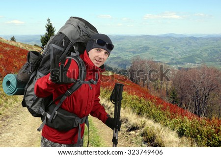 the Happy traveler equipped with a red jacket on the hillside raised in greeting hand