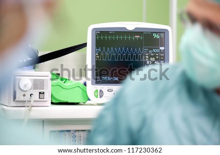 Cardiogram monitor in surgery while not recognizable doctor operates, focus on screen