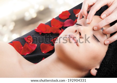 Beautiful woman receiving a facial massage lying on bed with rose petals.
