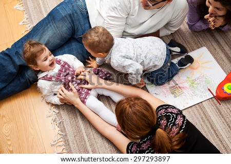 family group of five - two babies and three adults lying on the carpet, mom is tickling her daughter.